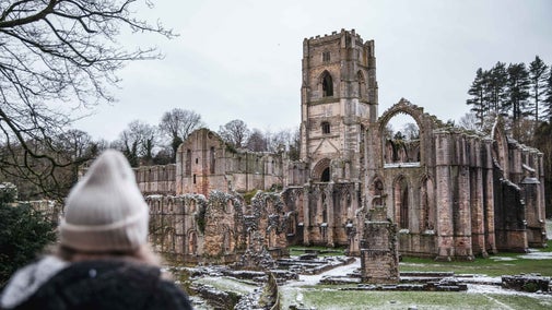 Person looking at Fountains Abbey from de greys walk on a snowy day